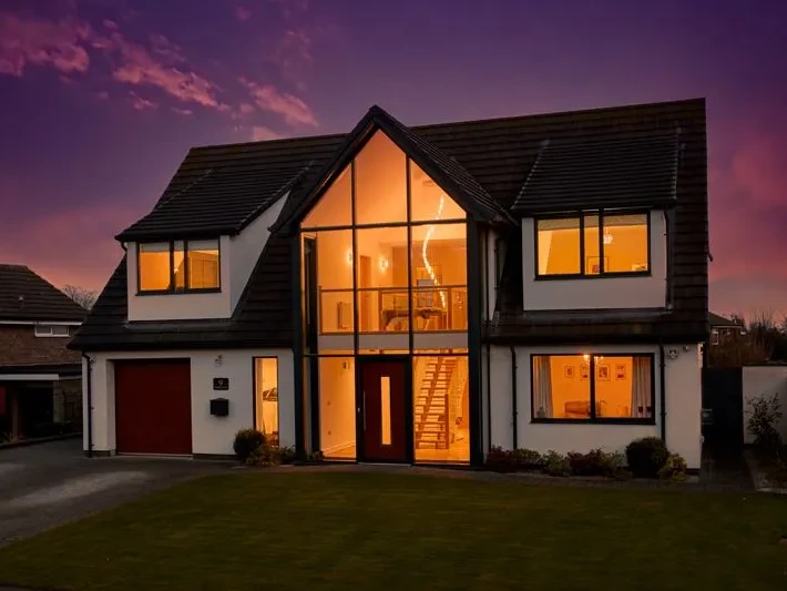 Front elevation at dusk of contemporary replacement dwelling in Copmanthorpe York, showing full-height six-metre glazed section and render finish — Fining Associates Architects York