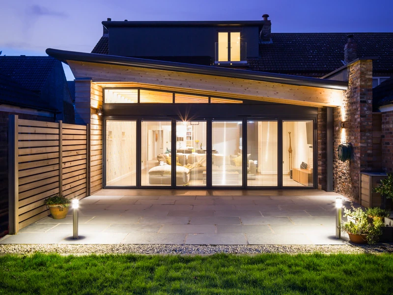 Panoramic dusk view of the illuminated contemporary rear extension at Barkers House, Hessay, showing zinc roof and cedar cladding