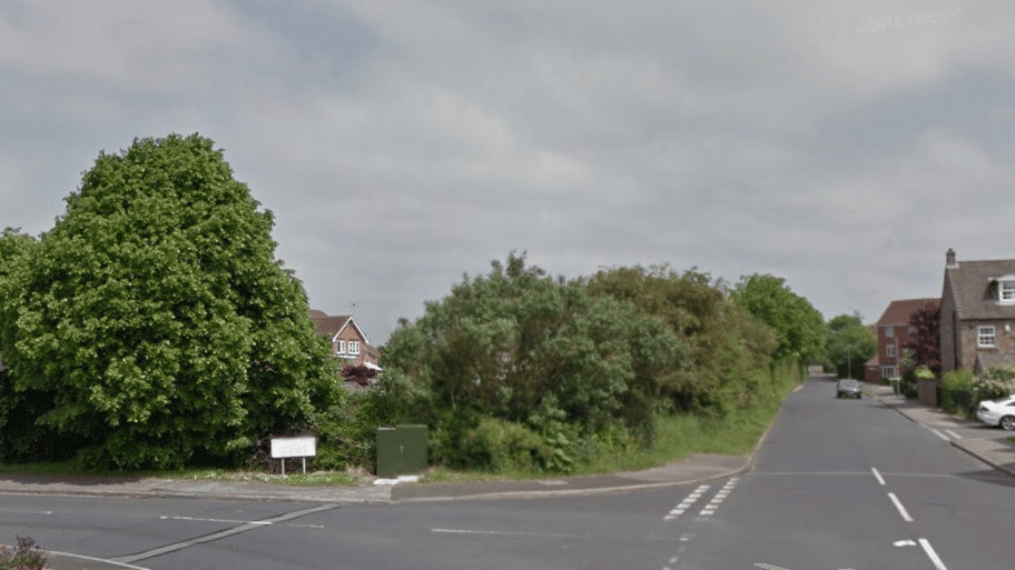 An animated before-and-after GIF of a residential infill development in Rawcliffe, York. The animation starts by showing the original site: an overgrown corner plot bounded by a large, unkempt hedge and mature trees. It then transitions to the completed project, revealing four new, modern semi-detached houses featuring landscaped front driveways, roof-mounted solar panels, and a new public footway, while retaining the large protected trees on the corner.