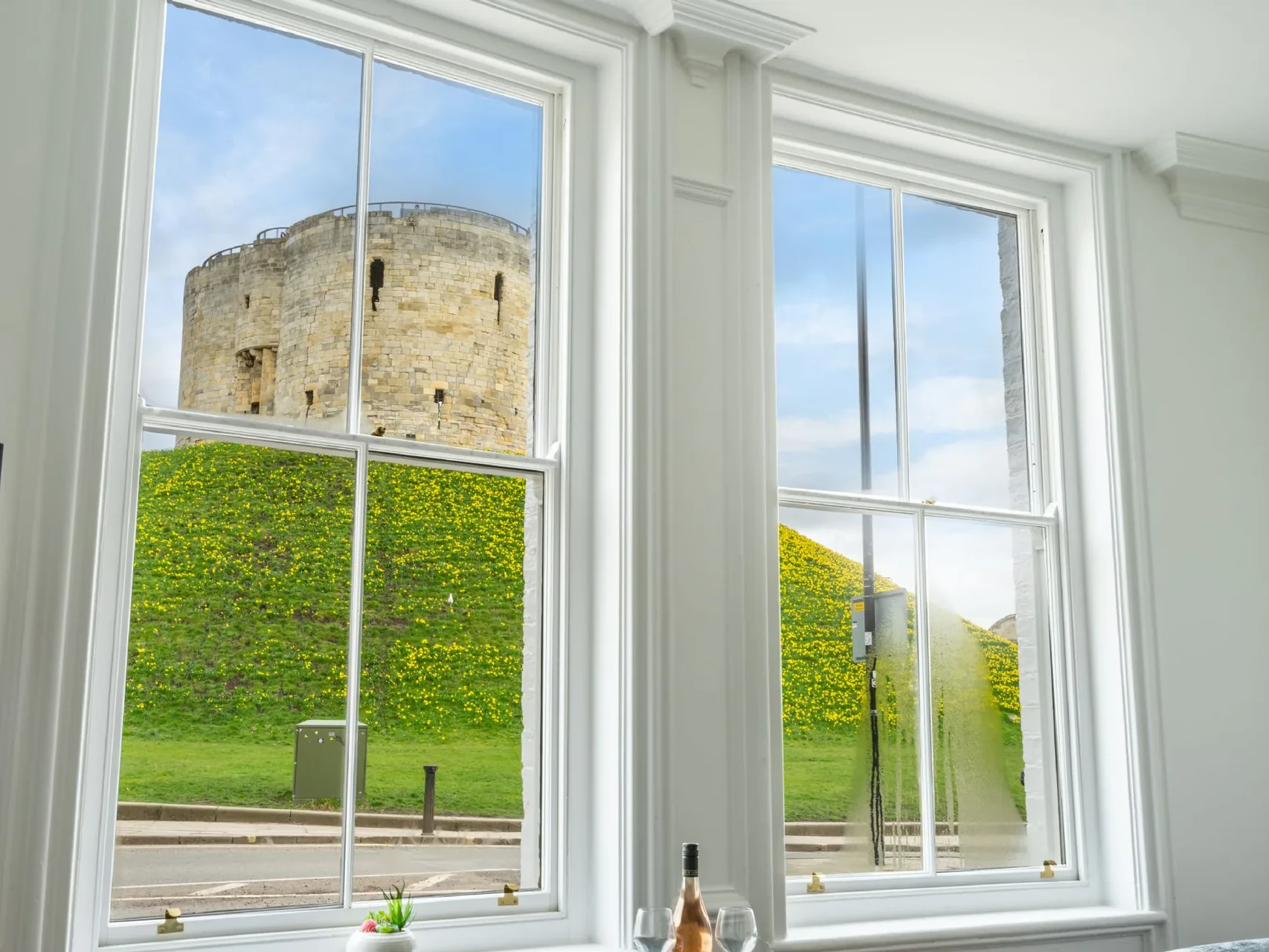 Direct view of Clifford's Tower and its wildflower-covered motte through original restored timber sash windows in a Grade II listed Victorian townhouse conversion, Tower Street York