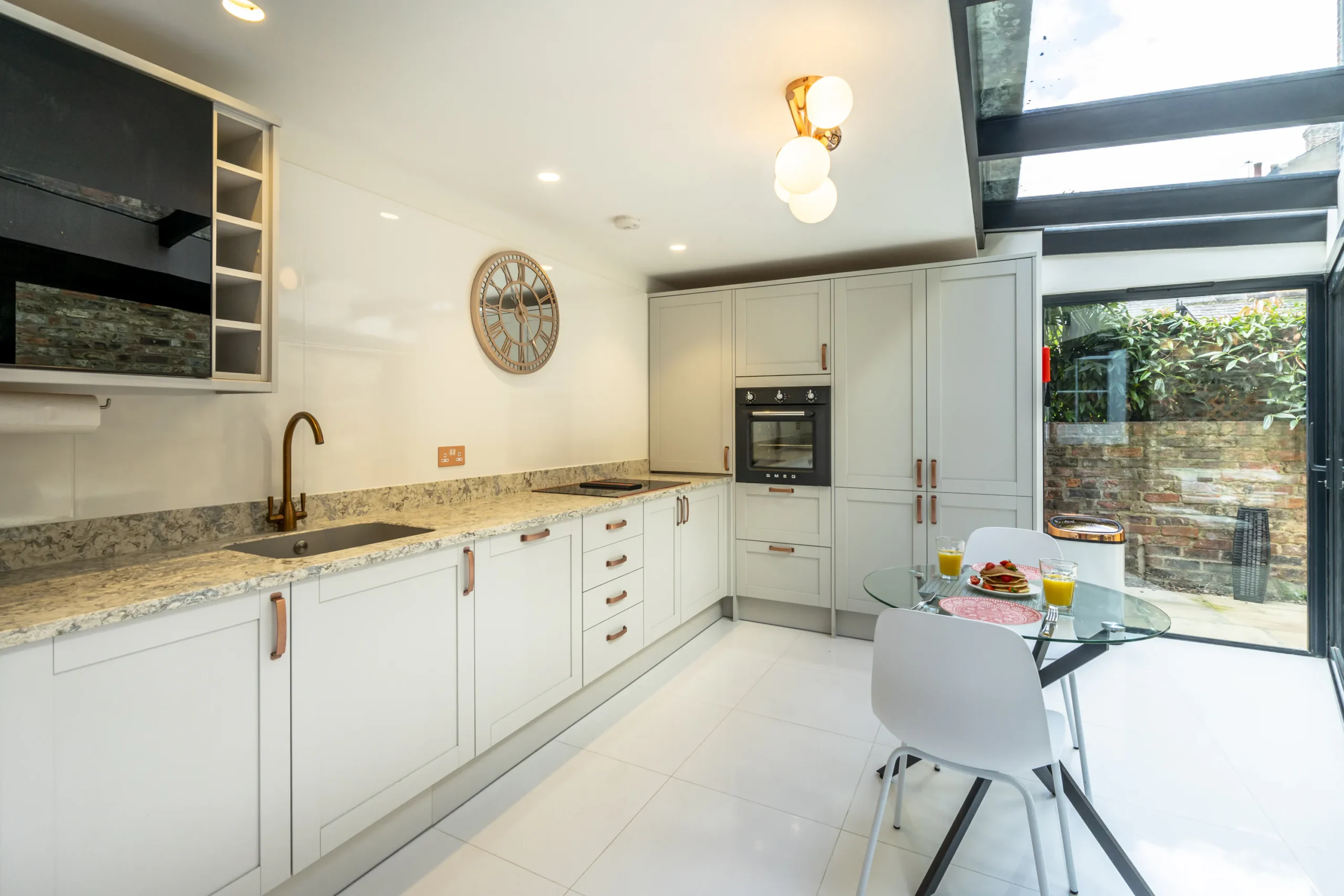 Light-filled kitchen in a contemporary rear extension to a Grade II listed townhouse in York, featuring shaker-style grey cabinetry, granite worktops, brass tap, Smeg oven, rooflight and sliding doors opening to a private courtyard