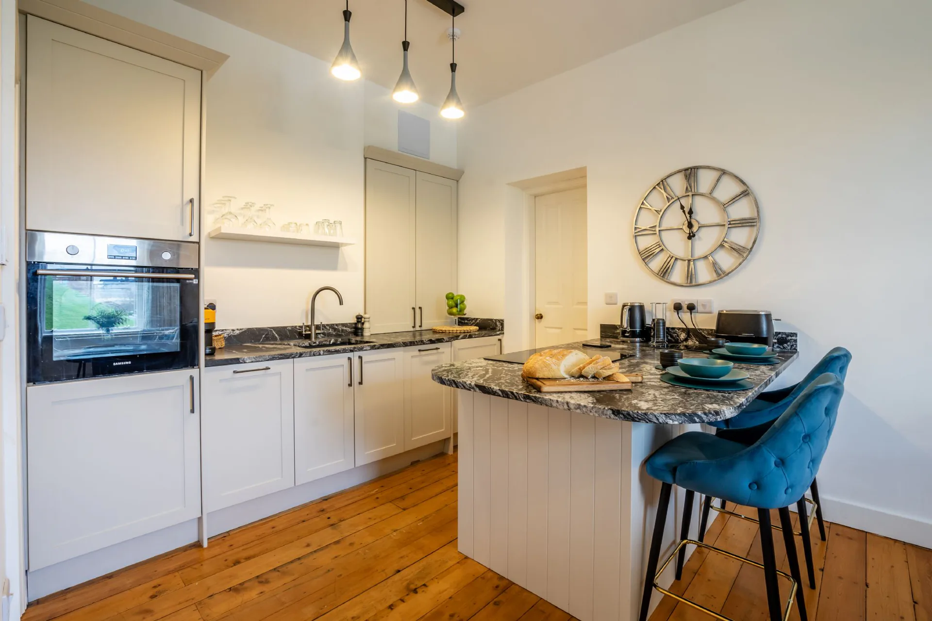 Contemporary shaker kitchen with dark marble worktops, breakfast island, teal velvet bar stools and pendant lighting over original pine floorboards in a Grade II listed Victorian townhouse conversion, York