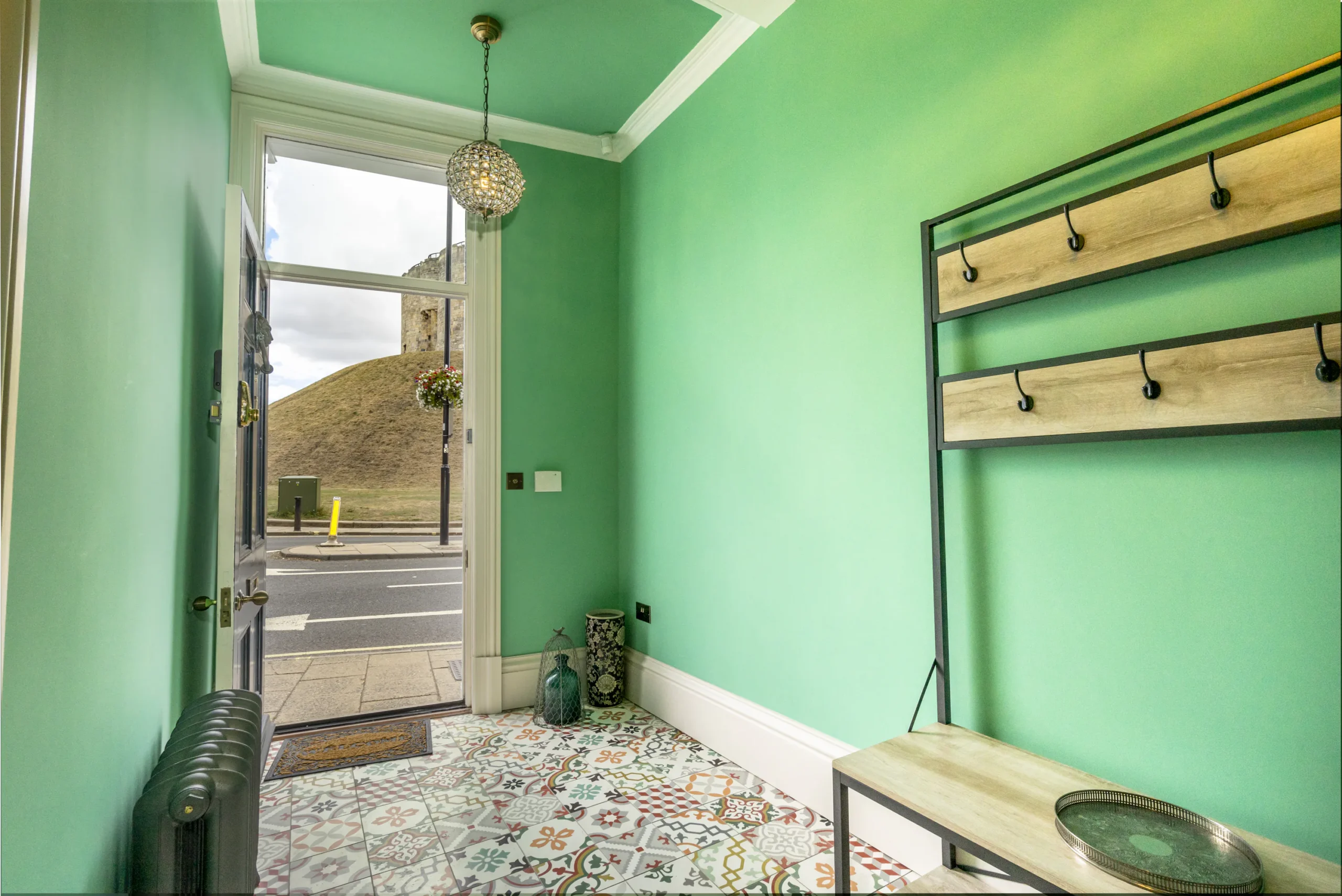 Renovated entrance hallway of a Grade II listed townhouse in York with mint green walls, encaustic patterned floor tiles, crystal pendant light and views towards Clifford's Tower