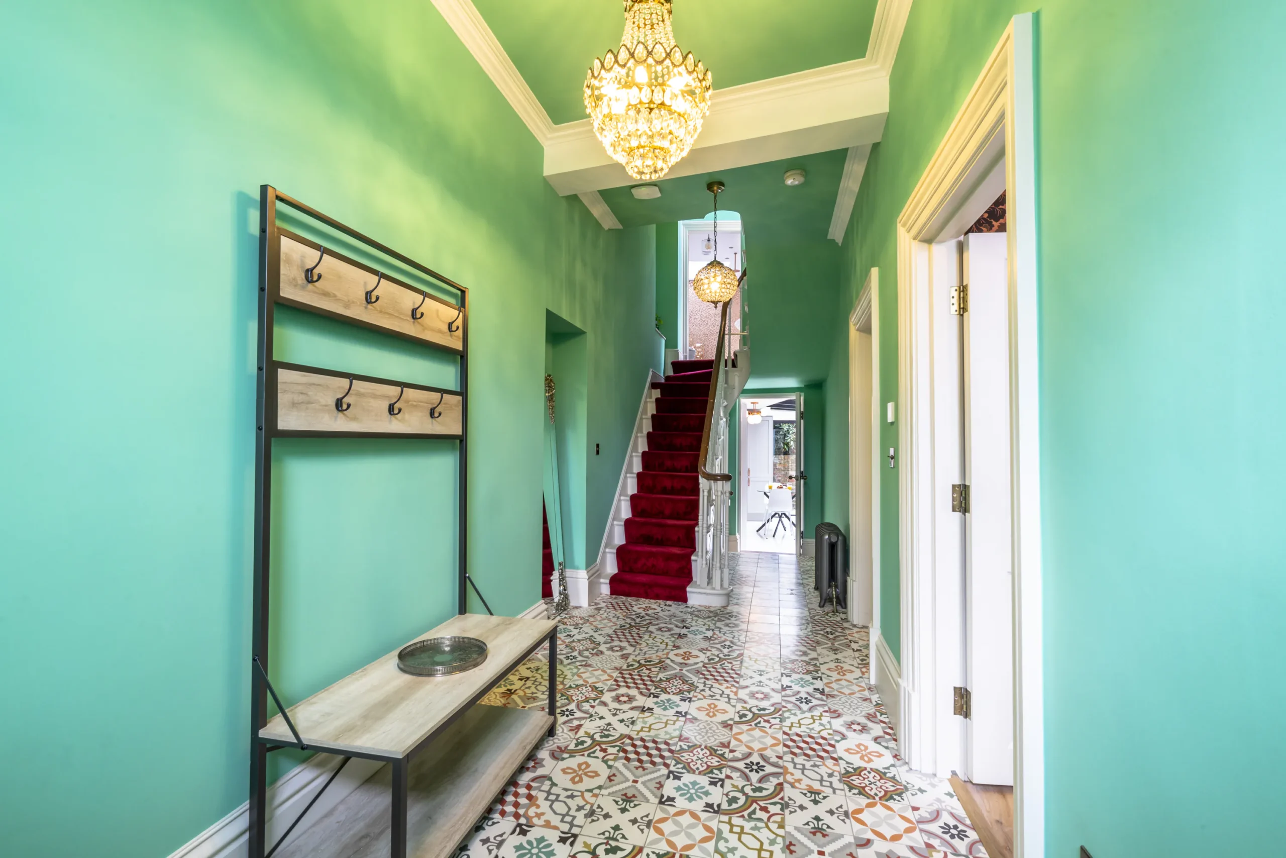 Grand hallway of a refurbished Grade II listed townhouse in York featuring encaustic floor tiles, mint green walls, ornate crystal chandelier and red-carpeted staircase leading to the contemporary rear extension