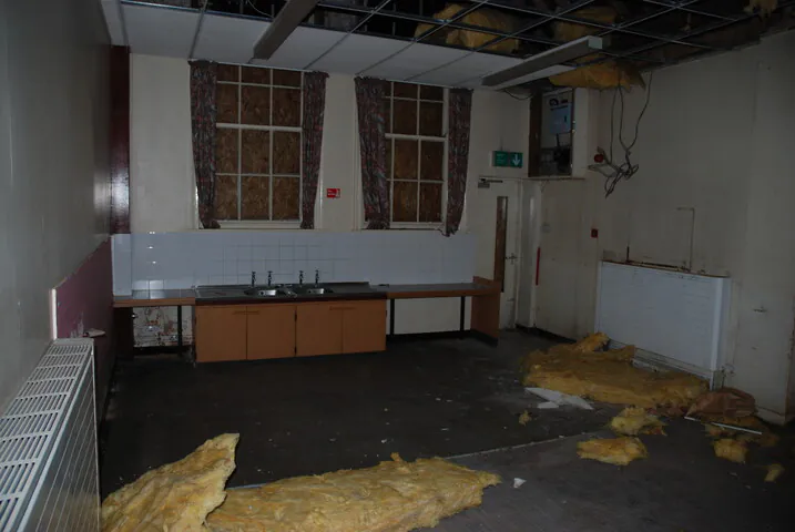 A darkened room in the old Shipton Street School with exposed insulation on the floor and boarded windows, showing the condition before the creation of double-height living spaces.