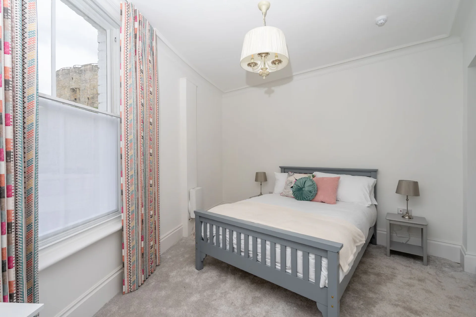 Bright double bedroom with grey wooden bed frame, chandelier and sash window overlooking Clifford's Tower in a Grade II listed Victorian townhouse conversion, Tower Street York