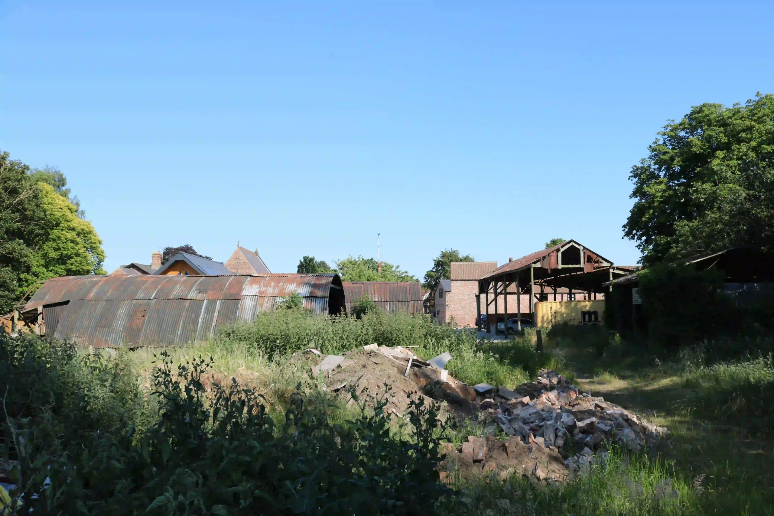 Derelict pole barn and Nissen huts at Model Farm, Upper Poppleton, with overgrown croft field and rubble in the foreground, before planning approval