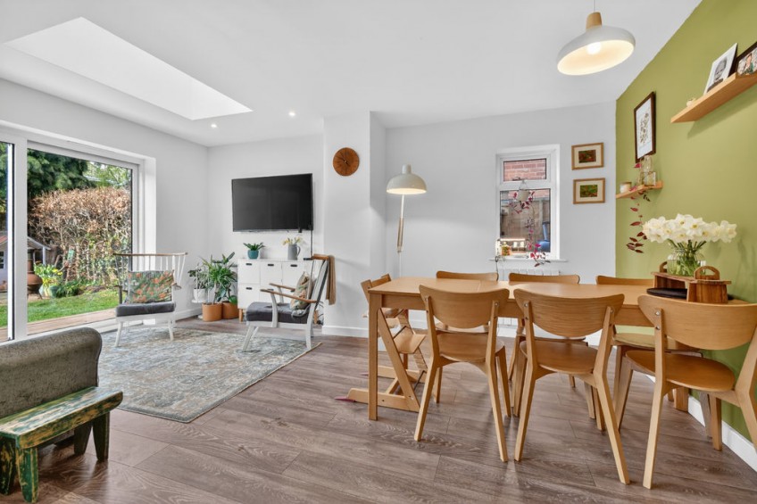 Spacious open-plan dining and living area featuring a wooden family table, green feature wall, and a modern roof lantern, added during a two storey front and rear extension.