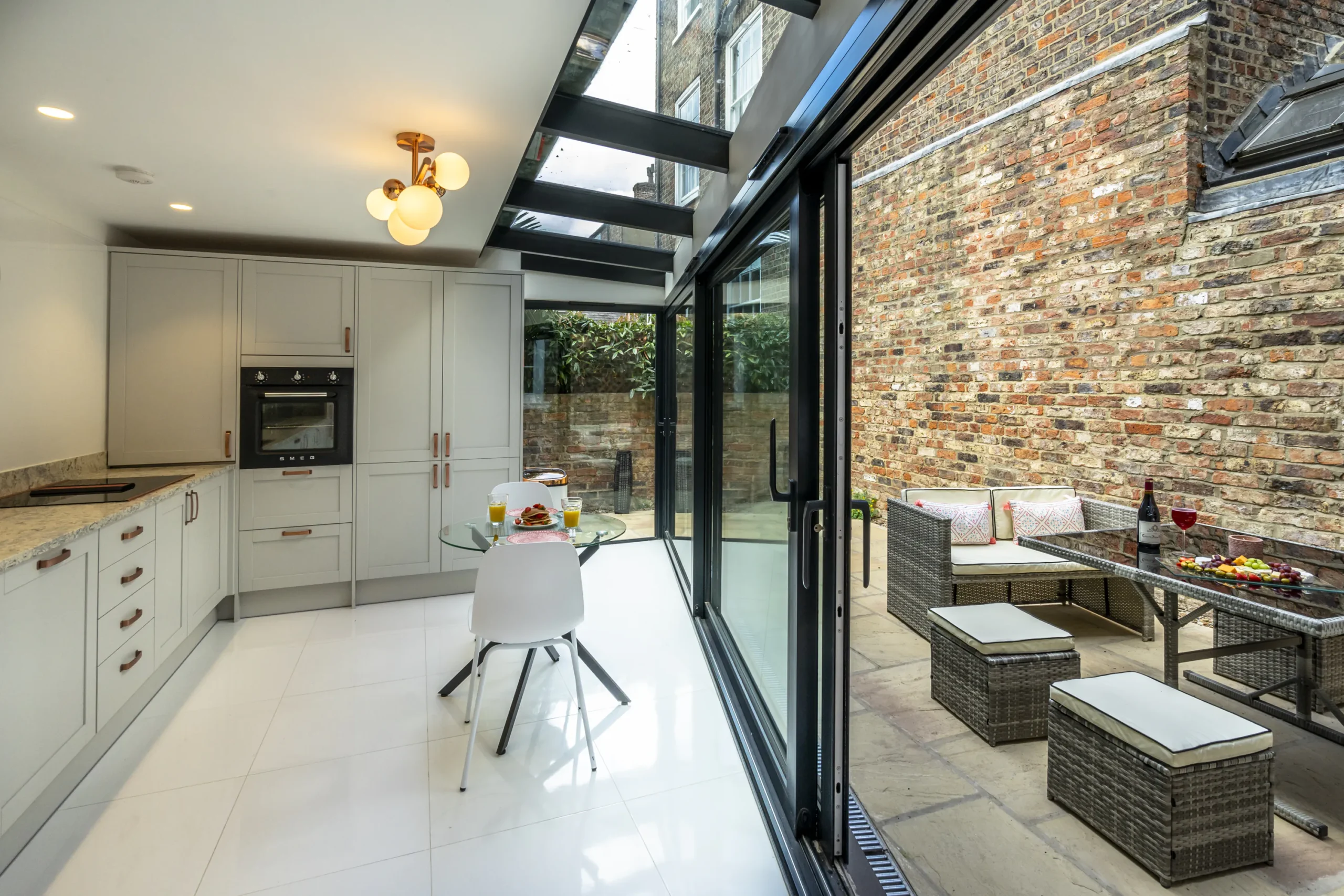 Open-plan kitchen dining area in a contemporary rear extension to a Grade II listed townhouse in York, with structural glass rooflight, aluminium sliding doors opening directly onto a private sandstone courtyard and exposed historic brick party wall