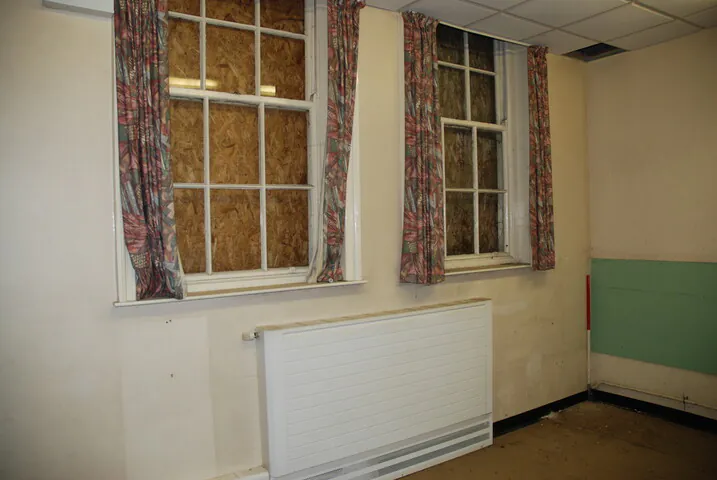 Tall Victorian sash windows boarded with plywood inside the old school, highlighting the original architectural features to be preserved during the listed building conversion.