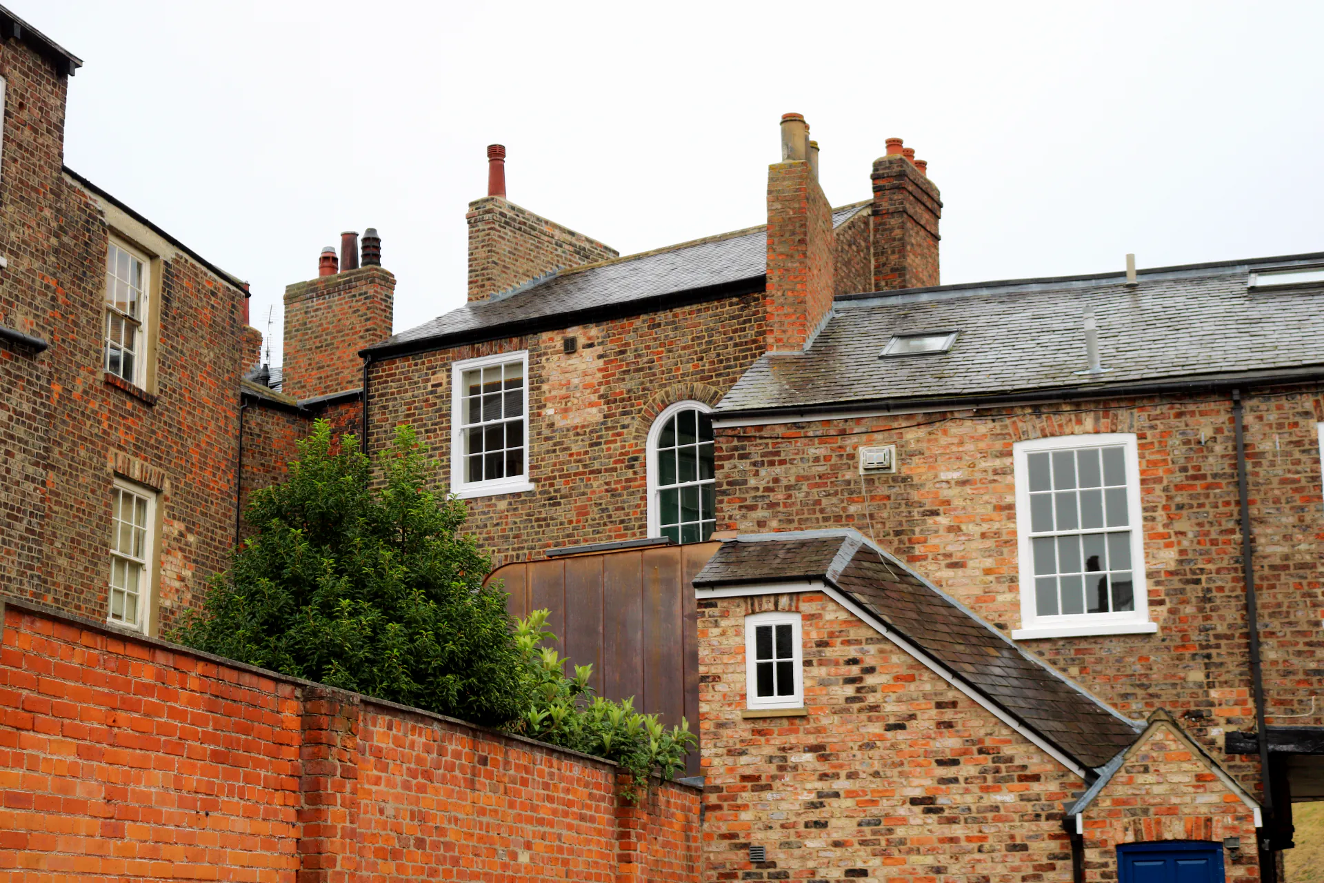 Rear exterior view of a Grade II listed townhouse in York showing the contemporary copper-clad rear extension nestled within the original Georgian brick rear elevation, with arched sash window, slate roofline and multiple period chimney stacks
