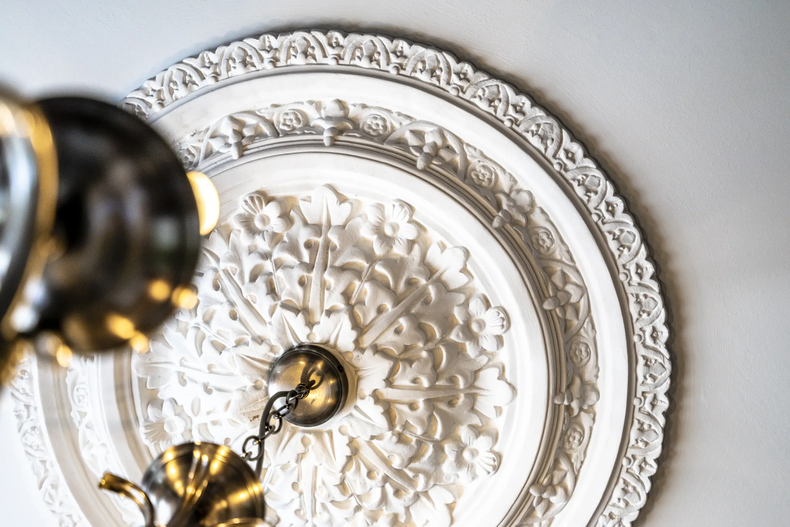 Close-up detail of an ornate restored plaster ceiling rose with floral and foliate decoration in a Grade II listed townhouse in York, with brass chandelier fitting