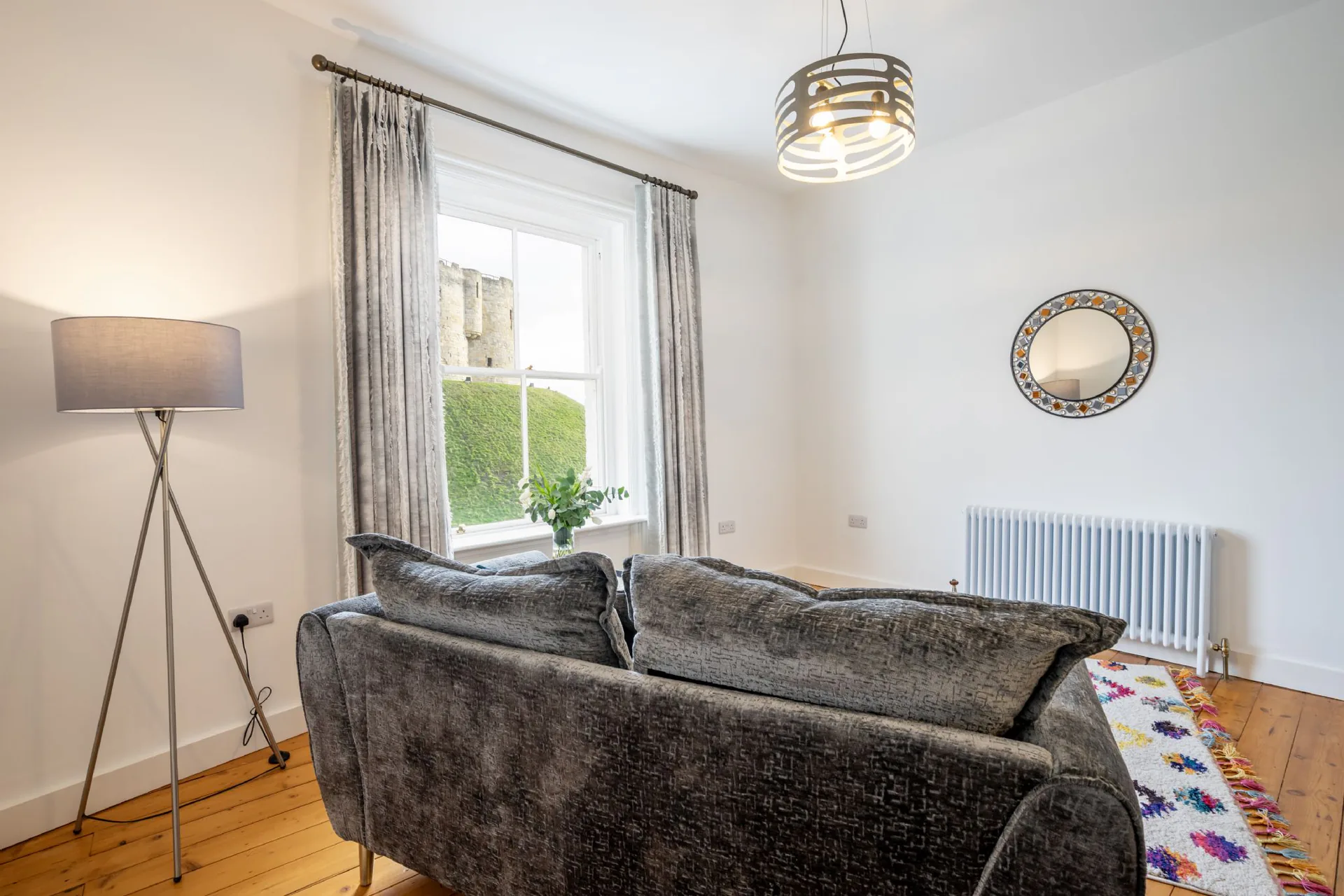 Sitting room with grey velvet sofa, tripod floor lamp and tall sash window overlooking Clifford's Tower in a Grade II listed Victorian townhouse converted to residential apartments, York