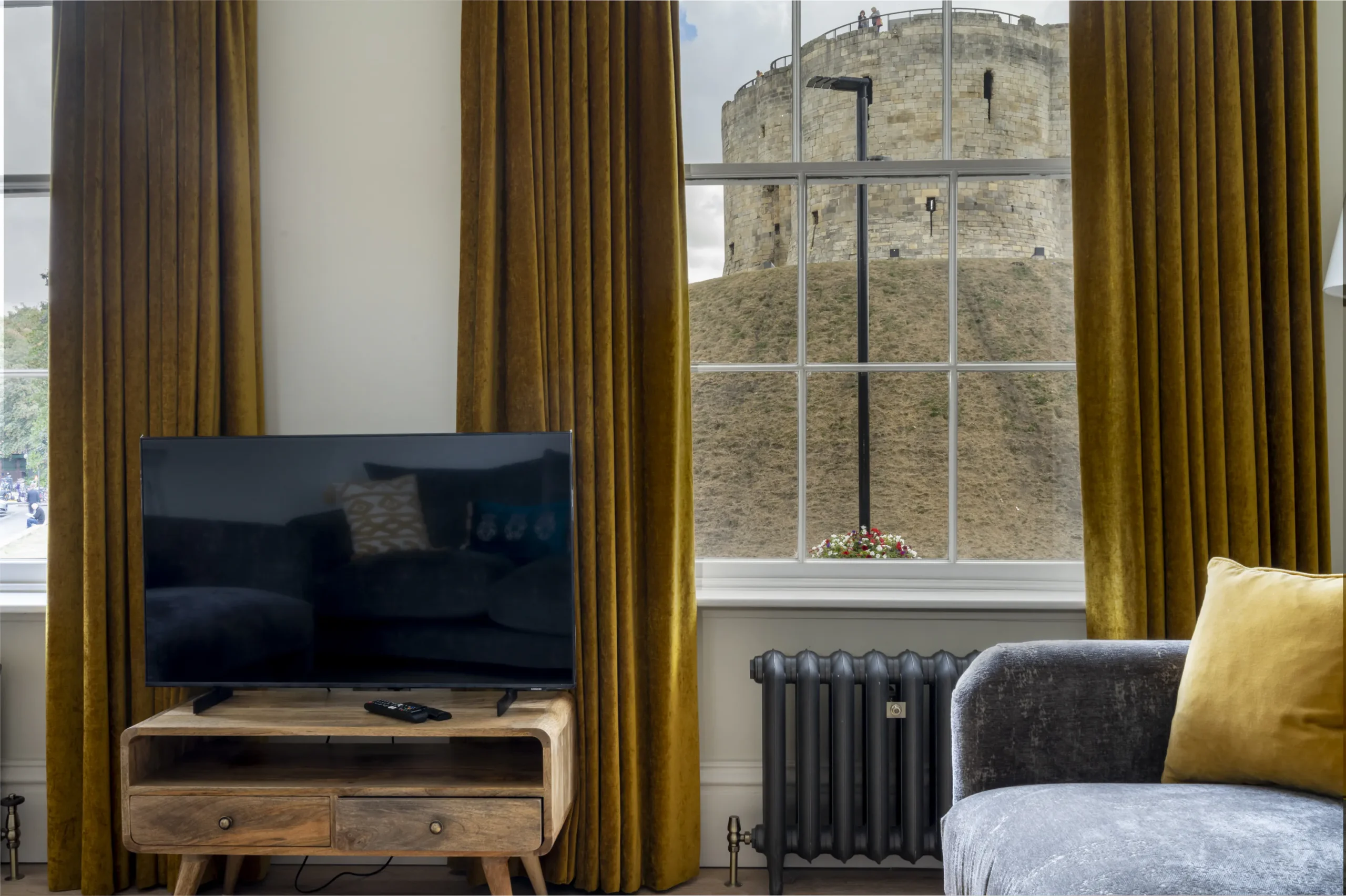 Sitting room of a refurbished Grade II listed townhouse on Tower Street York, with original sash window framing a direct view of Clifford's Tower, velvet mustard curtains, cast iron radiator and period cornicing