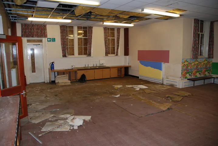 The dilapidated interior of a large classroom at Shipton Street School in York, showing damaged ceiling tiles, debris, and boarded-up Victorian windows before its residential conversion.
