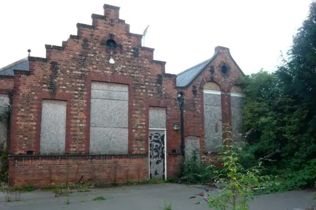 The boarded-up red brick exterior and gables of the derelict Shipton Street School in York, showing graffiti and overgrown weeds prior to its listed building conversion.