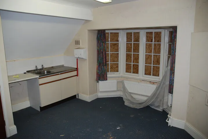 n upper-floor room with a boarded-up bay window and blue carpeting in the derelict Shipton Street School building before its brownfield residential development.