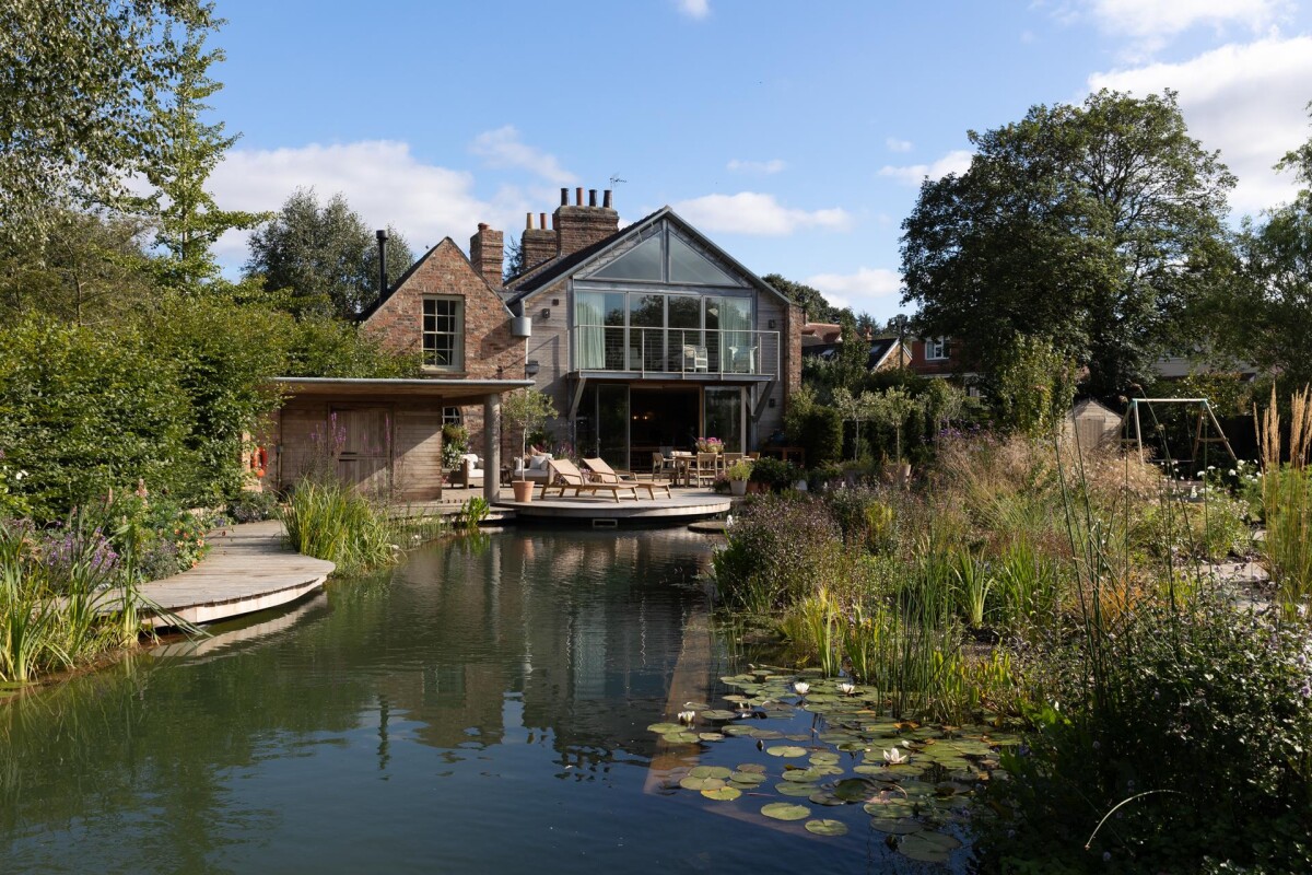 Double storey extension in Nether Poppleton conservation area York at dusk, with cedar cladding, glazed gable, natural swimming pool and lily pond in foreground