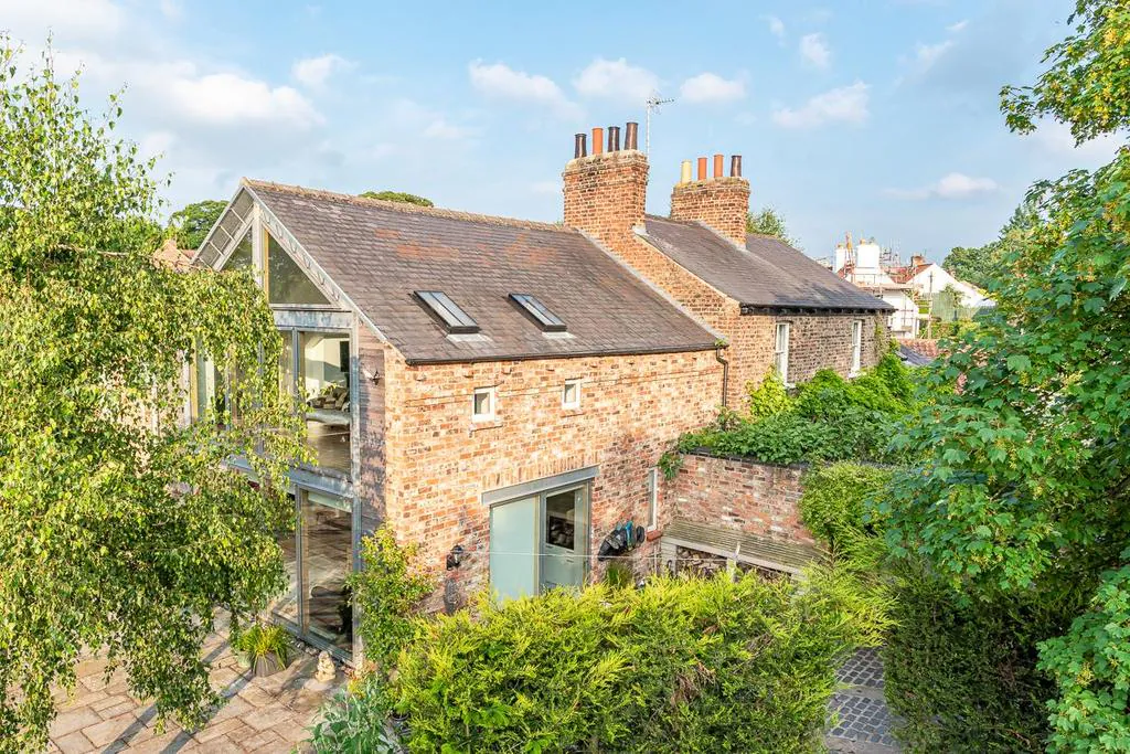 Glazed gable double storey extension adjoining original Victorian brick cottage in Nether Poppleton conservation area, York, with village roofscape beyond