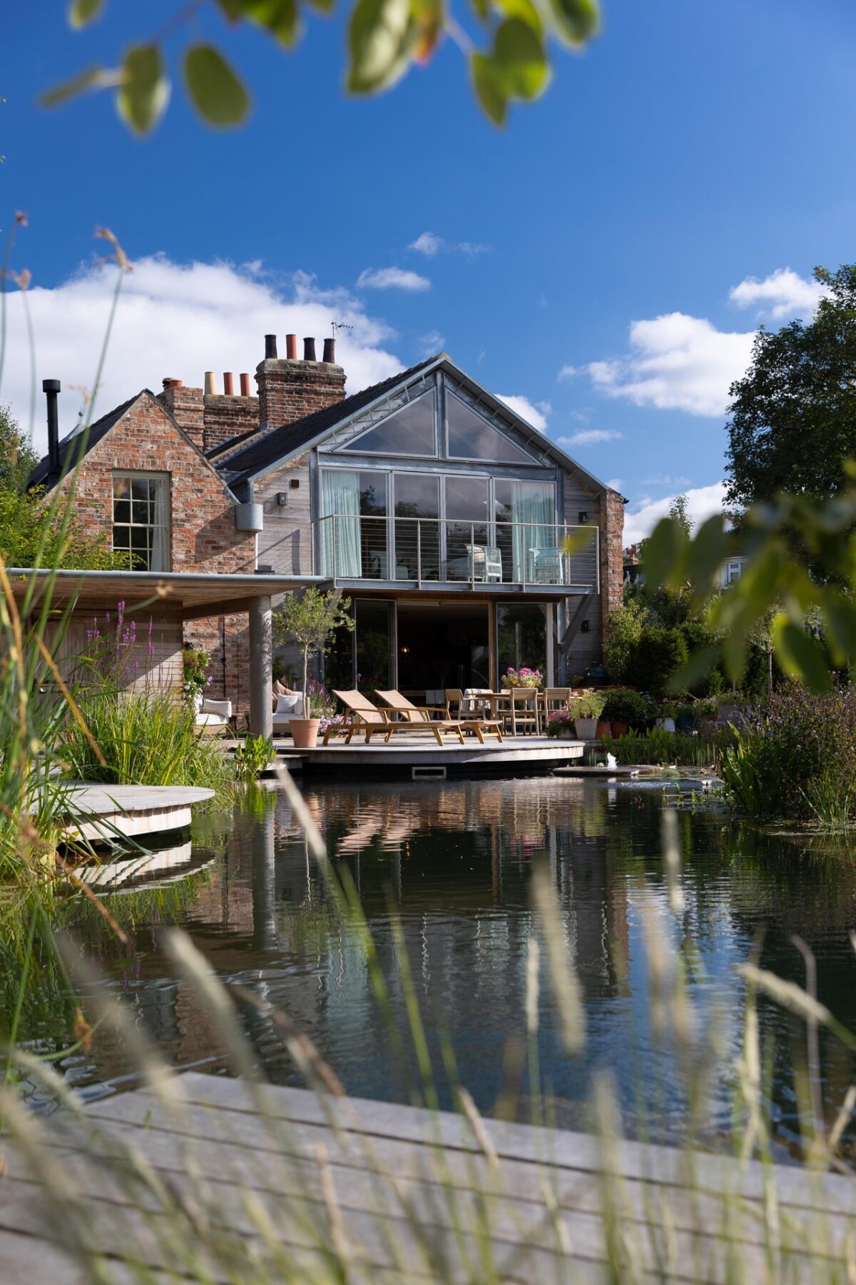 Glazed gable of double storey extension in York conservation area reflected in natural pool, original Georgian brick cottage behind, Nether Poppleton