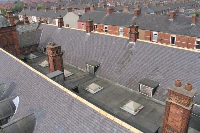 A high-angle view of the original slate roof, skylights, and brick chimneys of the Grade II listed Shipton Street School prior to architectural restoration.