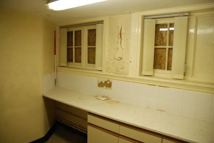 A derelict internal area of the 1890 Walter Brierley designed school, showing peeling paint, white tiled splashbacks, and boarded windows before restoration.