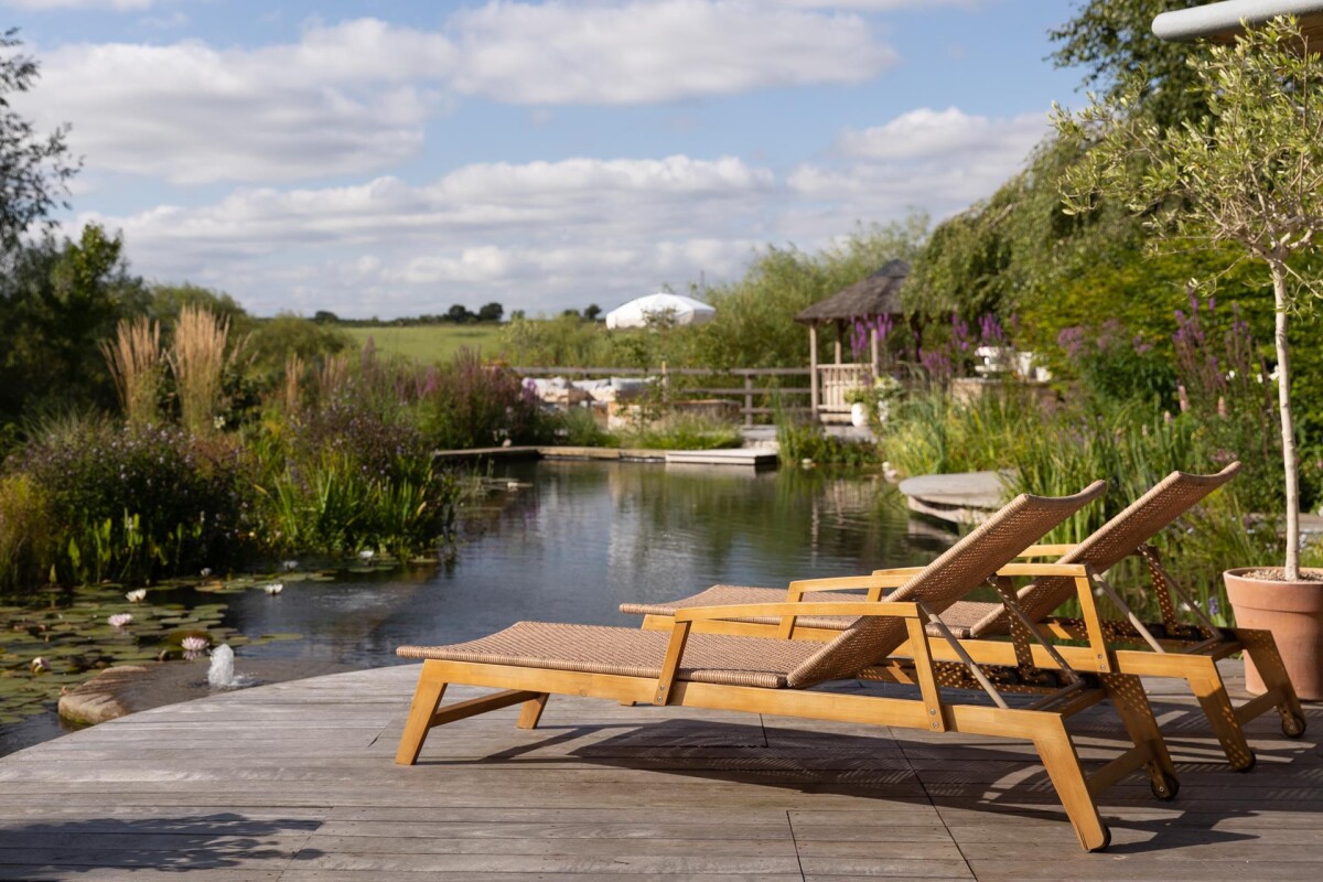 Riverside decking with sun loungers beside natural swimming pool, period property extension in Nether Poppleton York with open countryside beyond