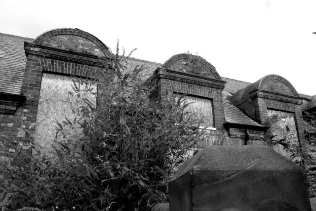 A black and white close-up of the arched brickwork and boarded classroom windows of the Grade II listed school designed by architect Walter Brierley.