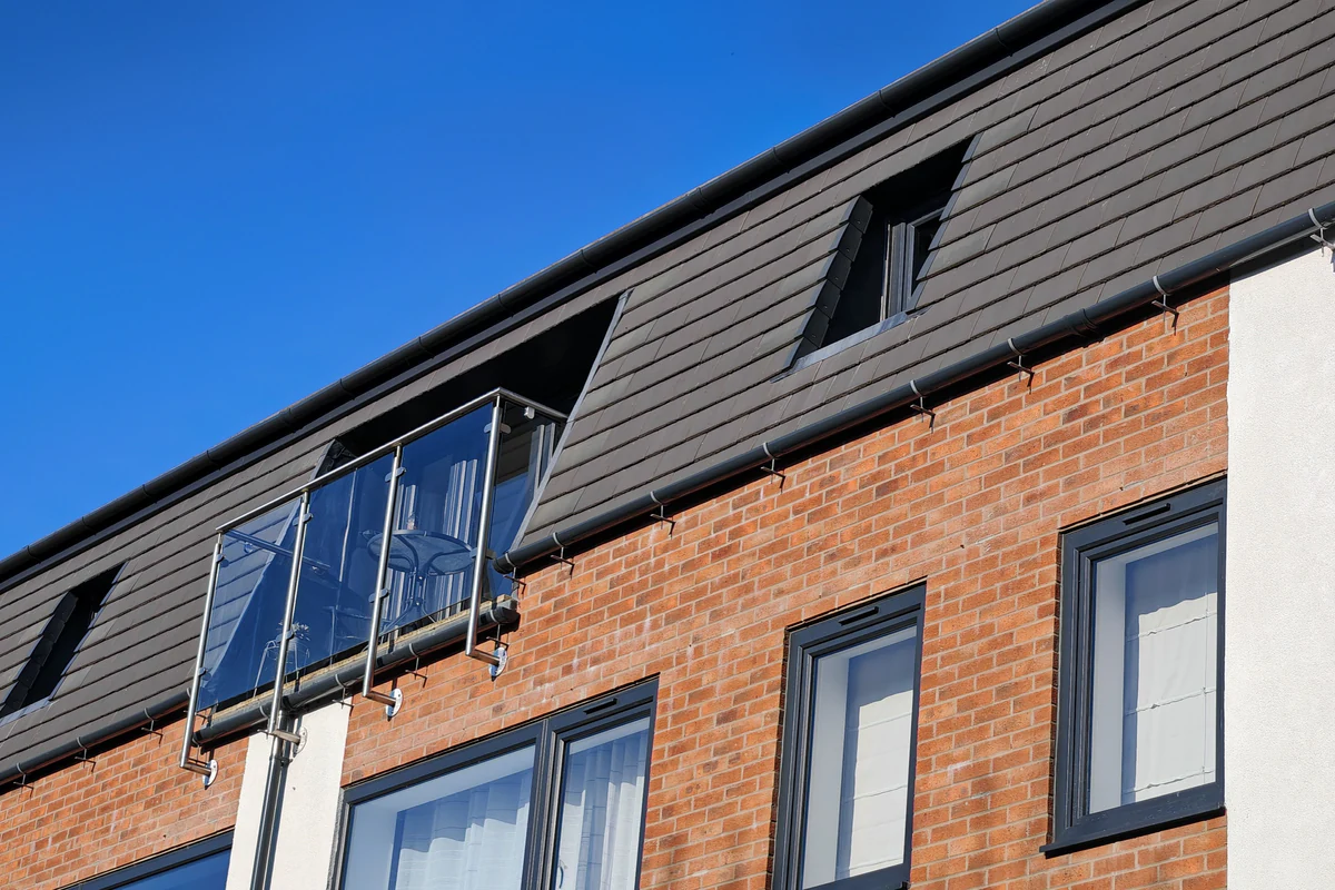 West elevation of Hawthorn Street Apartments, Layerthorpe York, showing a glass Juliet balcony, self-coloured white render panels, and dark slate mansard roof with recessed angled dormers — a fabric-first sustainable residential design by Fining Associates.