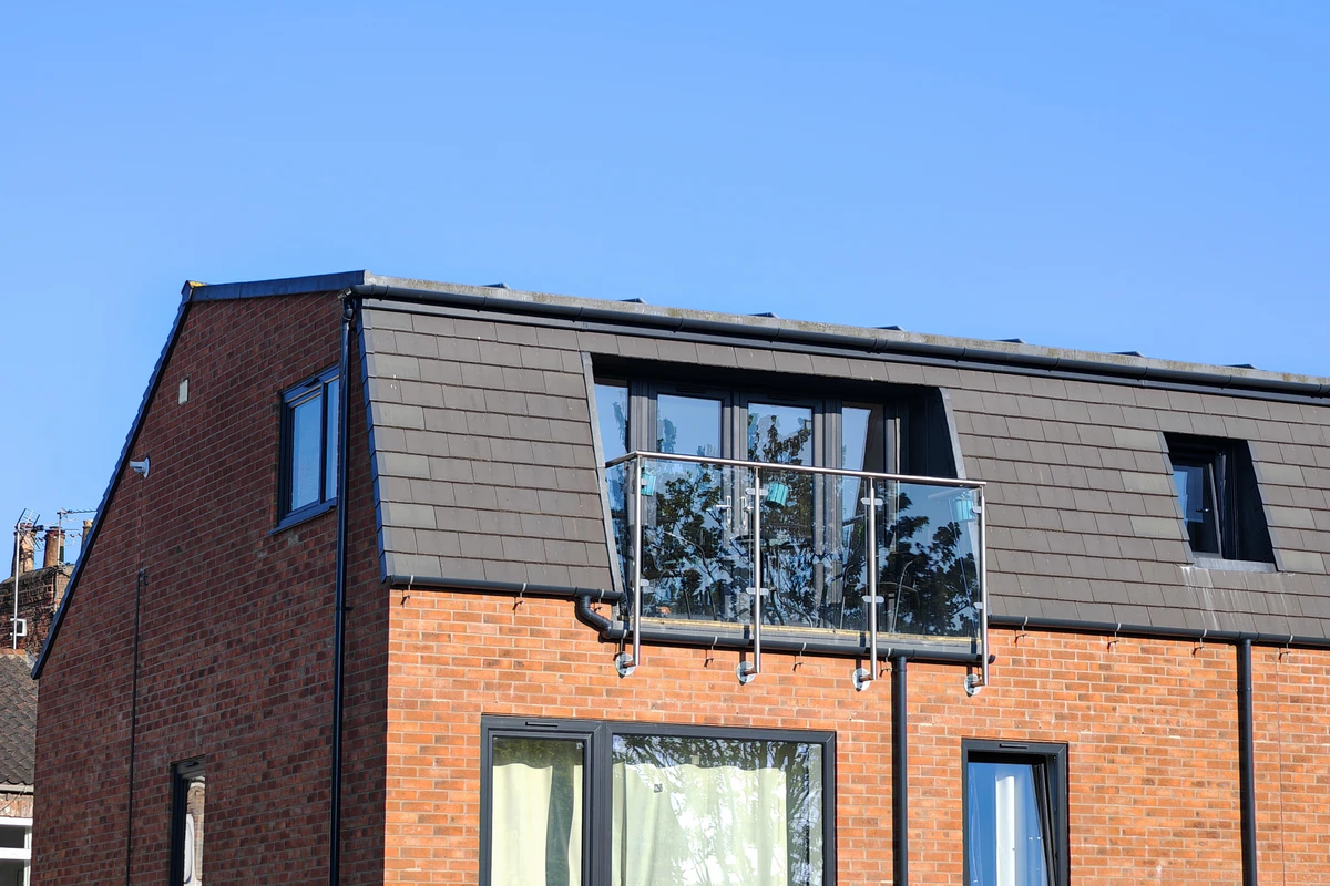 Detail of the glass and stainless steel Juliet balcony set against the dark grey slate mansard roof of Hawthorn Street Apartments, York — private outdoor space for top-floor apartments in this 10-unit brownfield residential development by Fining Associates architects.