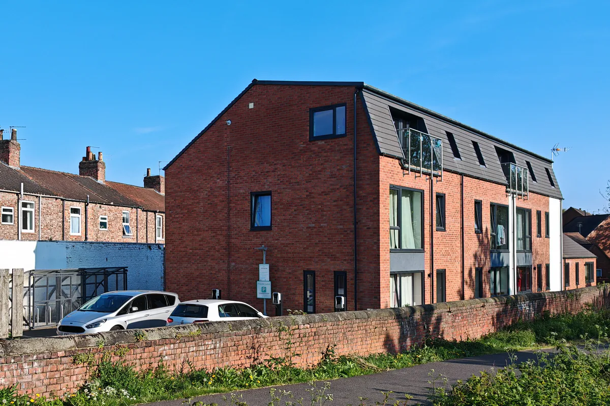 Wide view of Hawthorn Street Apartments, Layerthorpe York, from Foss Islands cycleway frontage, showing the completed brownfield new-build with EV charging spaces, secure covered cycle store and red-brick mansard roof apartment building designed by Fining Associates chartered architects.