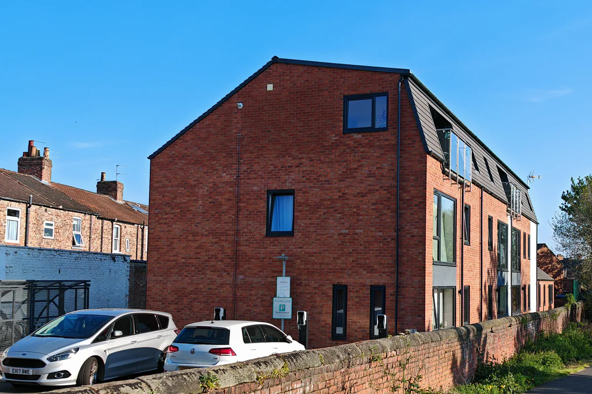 North elevation and parking court of the Hawthorn Street apartment development, Layerthorpe York, showing EV charging points serving three on-site spaces and the red-brick contemporary new-build replacing the former Glen Garage brownfield site.