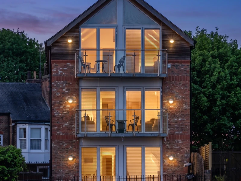 Three-storey new-build apartment block with lit interiors, glazed gable and stacked balconies at dusk, designed by a residential architect in York